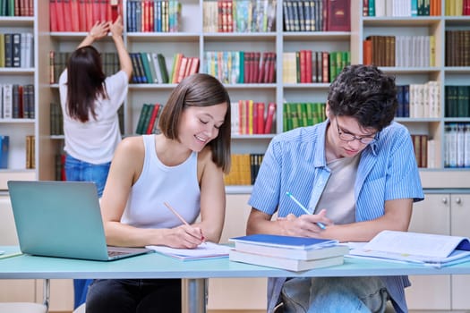 Young male and female students sitting at desk in college library, with books, notebooks, studying, preparing for exams. Knowledge, education, youth, college university concept
