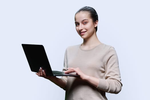 Teen girl high school student using laptop looking at camera on white studio background. Technology, e-learning, education, adolescence, youth concept.