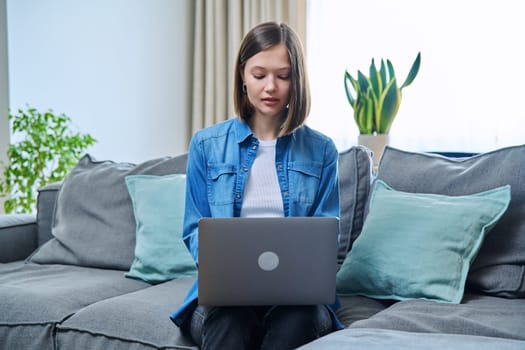 Young woman sitting on sofa typing on laptop. Internet technologies for study leisure, female freelancer working remotely, university student watching online course, e-learning, rest communication