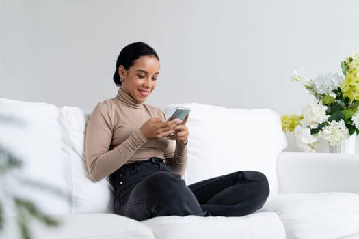 Relaxed young African American woman using crucial mobile phone on sofa couch in living room at home