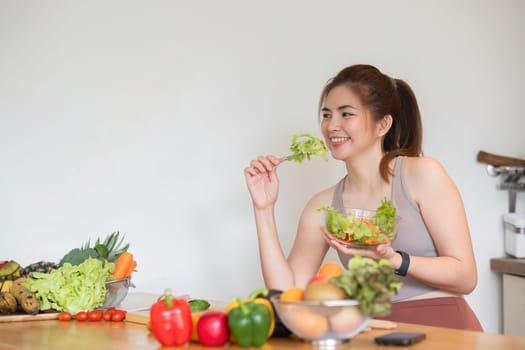 Healthy Asian woman takes care of her health by eating vegetable and fruit salad, adding vitamins in the kitchen..