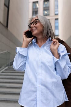 well-groomed slender mature business woman with gray hair dressed in a brown suit walks and talks on the phone.