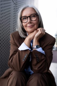 portrait of a well-groomed slender senior business woman with gray hair dressed in an elegant brown jacket over a shirt.