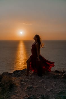 Woman sunset sea red dress, back view a happy beautiful sensual woman in a red long dress posing on a rock high above the sea on sunset