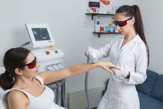 Woman in a beauty salon removes hair from her arm with laser epilation