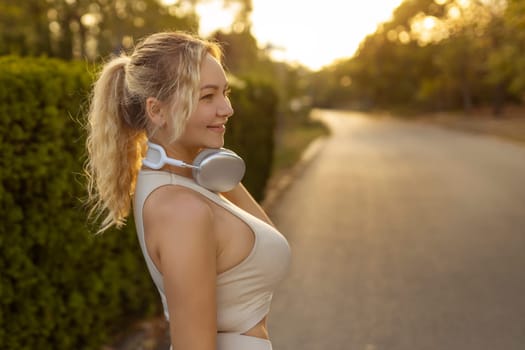 Portrait of fit girl preparing for running in workout clothes looking at camera smiling. Beautiful happy sportswoman enjoying doing sports listening to music using headphones. Music concept