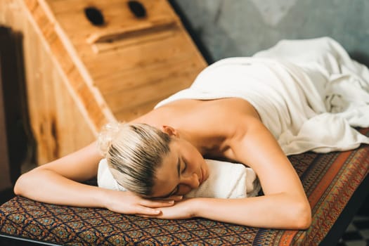 Beautiful relaxing caucasian woman lie on spa bed in front of wooden sauna cabinet. Young and healthy woman waiting for massage treatment in warm traditional spa room. Tranquility.