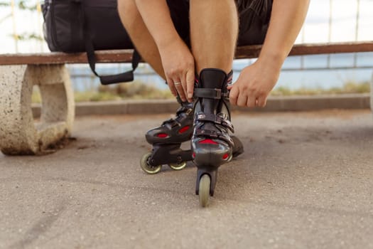 Legs of young man putting on roller skates in the park.