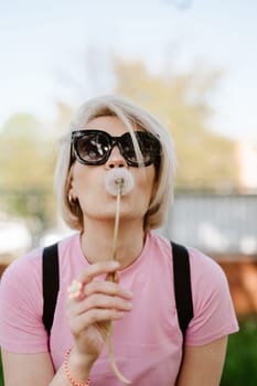 Portrait of a beautiful young woman blowing dandelion flower. Shallow dof