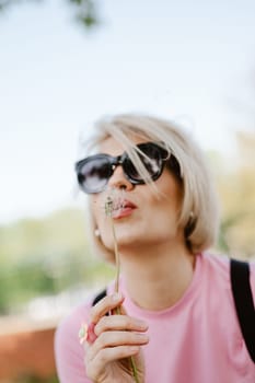 Portrait of a beautiful young woman blowing dandelion flower. Shallow dof