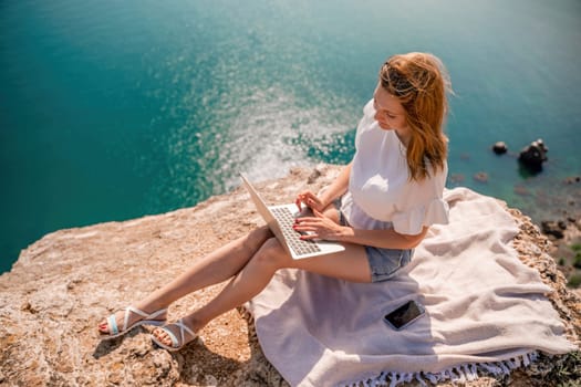 Freelance woman working on a laptop by the sea, typing away on the keyboard while enjoying the beautiful view, highlighting the idea of remote work