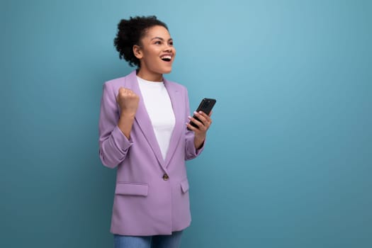 young successful hispanic brunette leader woman with curly hair rejoices holding a smartphone in her hand.