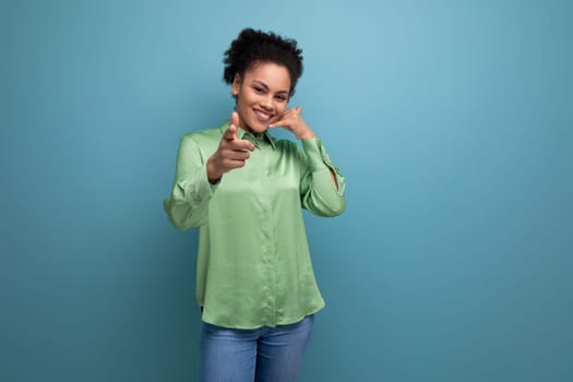 young female model with curly black hair dressed in a green blouse points with her hand at an advertisement on an isolated background with copy space.