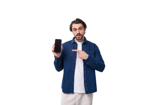 young european brutal brunette man with a cool hairstyle dressed in a denim shirt shows the screen of the phone vertically. e-business concept.