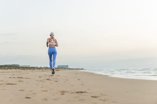 sportive woman running along beautiful sandy beach, healthy lifestyle, enjoying active summer vacation near the sea. High quality photo