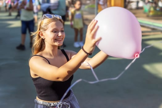 A teenage girl of European appearance happily poses with a large pink balloon in the city. High quality photo