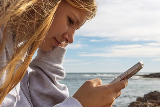 portrait of a teenage girl with a piercing in the nose sitting near the sea and the girl looks at the phone. High quality photo