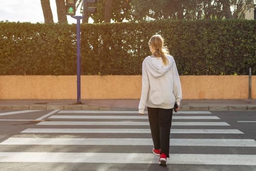 teenage girl in casual clothes crosses the road at a pedestrian crossing with her back to the camera. High quality photo