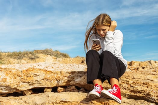 portrait of a teenage girl sitting near the sea and the girl looks at the phone. High quality photo