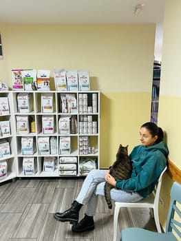 Young woman with a tabby cat on her lap sits on a chair in a veterinary clinic. High quality photo