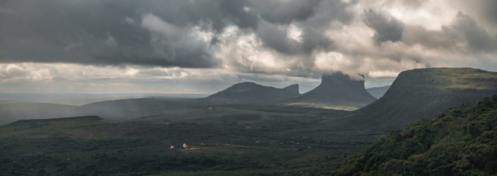 Stunning snapshot of Chapada Diamantina with local homes, large rocky peaks, mesetas, stormy clouds, and interplay of light and shadow.