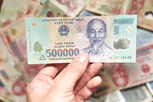 Male hand holds a fan of Vietnames Dong banknote, the currency of Vietnam. Close up Polymer Money of Vietnam. 500000 Dong or VND in male hand. In front a portrait of Ho Chi Minh. Plastic banknotes. High quality photo