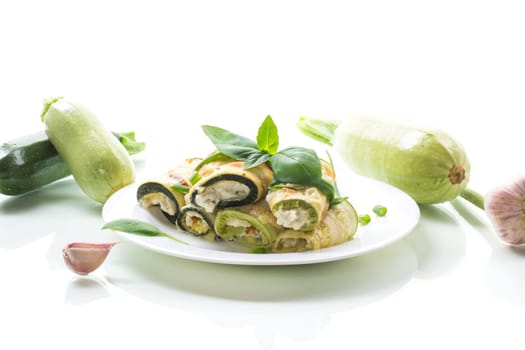 cooked zucchini rolls stuffed with cheese inside, in a plate isolated on white background
