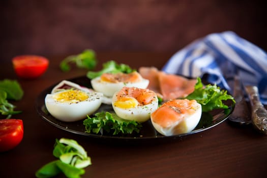 boiled eggs with salted red fish, herbs and seasonings in a plate on a wooden table.