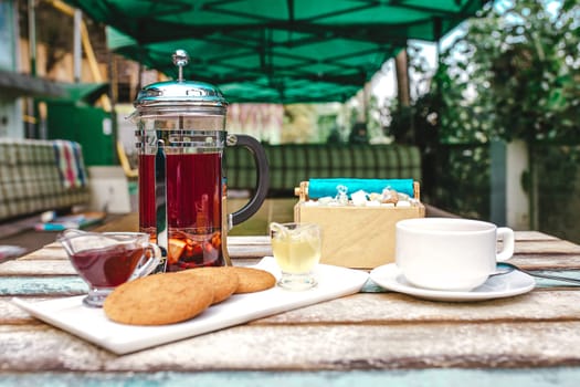 glass teapot tea and cookies on a wooden table outside.