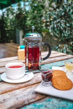 glass teapot tea and cookies on a wooden table outside.