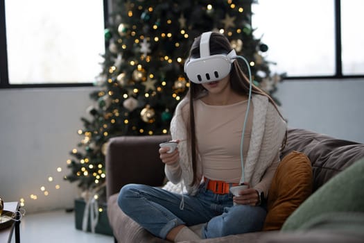 Engrossed in the comfort of a Christmas atmosphere at home, a stylish young woman dons a virtual reality headset. High quality photo