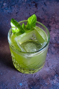 top view of a green cocktail in a glass with ice and a mint leaf on a textured background.