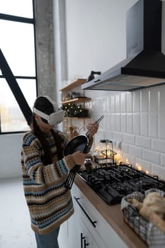 In the festive kitchen, a beautiful and stylish girl is cooking following a recipe with the aid of a virtual reality headset. High quality photo