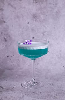 turquoise cocktail with a flower on a gray background.
