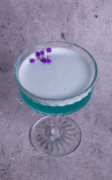 turquoise cocktail with a flower on a gray background.