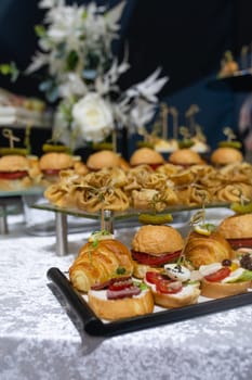 Croissants, burgers and various snacks on stands on the buffet table.