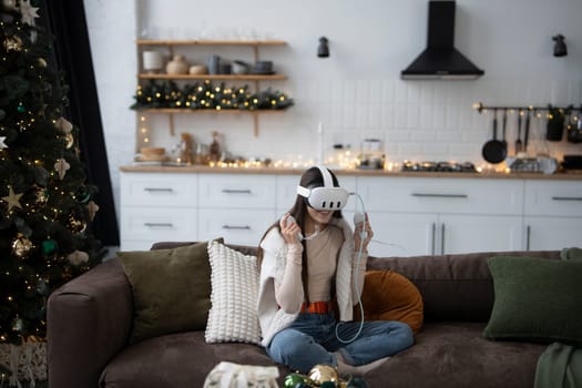 Enjoying a festive Christmas atmosphere at home, a stylish young woman is in a virtual reality headset. High quality photo