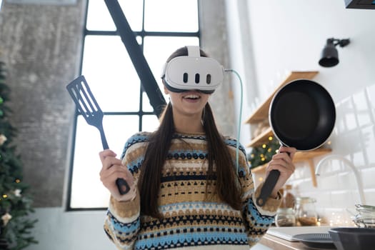 In the kitchen, a lovely young woman cooks while wearing a virtual reality headset. High quality photo