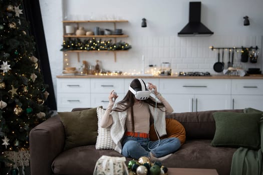A stylish young woman in a cozy Christmas atmosphere at home, wearing a virtual reality headset. High quality photo