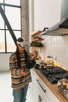 A stylish and beautiful girl is preparing a recipe in the Christmas kitchen while wearing a virtual reality headset. High quality photo