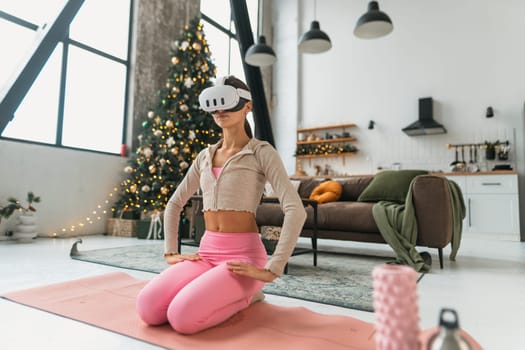 Engaged in virtual reality, a young lady in pink attire does yoga poses near a Christmas tree. High quality photo