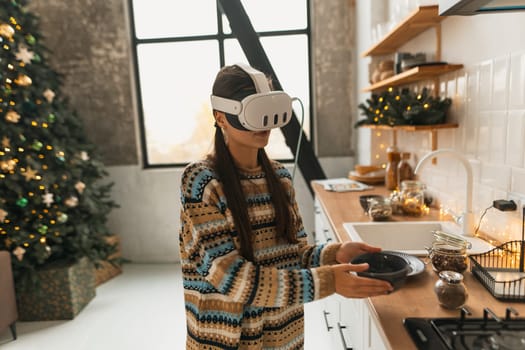 Engaged in holiday cooking, a beautiful and stylish girl uses a virtual reality headset for the recipe in the Christmas kitchen. High quality photo