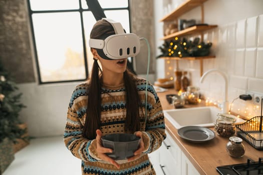 A beautiful and stylish woman is cooking in the Christmas kitchen using a virtual reality headset to follow a recipe. High quality photo