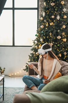 Enjoying a festive Christmas atmosphere at home, a stylish young woman is in a virtual reality headset. High quality photo