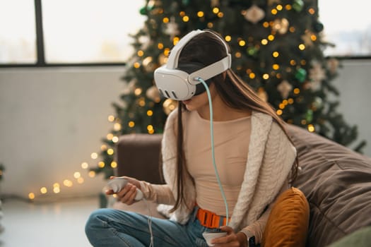 Relaxing in a homey Christmas environment, a trendy young lady sports a virtual reality headset. High quality photo