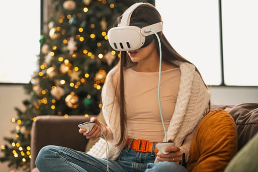 Surrounded by a comfortable Christmas vibe at her place, a stylish young woman is in a virtual reality headset. High quality photo