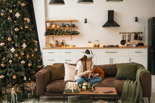 Amidst a warm Christmas ambiance at her place, a stylish young woman is seen in a virtual reality headset. High quality photo