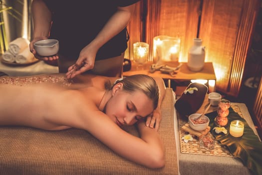 Woman customer having exfoliation treatment in luxury spa salon with warmth candle light ambient. Salt scrub beauty treatment in Health spa body scrub. Quiescent