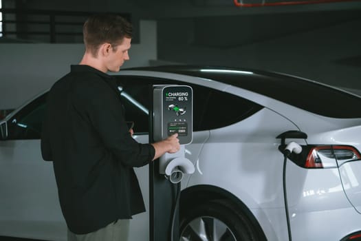 Young man travel with EV electric car to shopping center parking lot charging in downtown city showing urban sustainability lifestyle by green clean rechargeable energy of electric vehicle innards