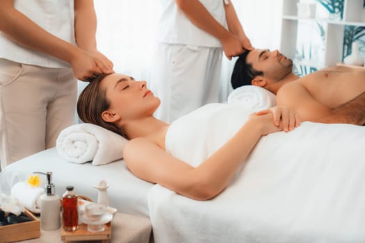 Caucasian couple enjoying relaxing anti-stress head massage and pampering facial beauty skin recreation leisure in dayspa modern light ambient at luxury resort or hotel spa salon. Quiescent